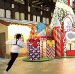 a person is standing in front of a gingerbread house with presents in front of it