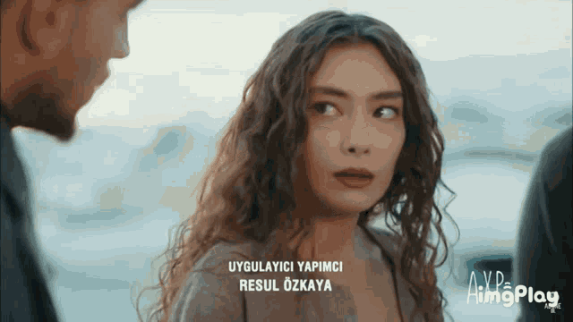 a woman with curly hair is standing next to a man and says " uygulamayici yapimci " on the bottom