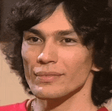 a close up of a man 's face with a red shirt on and a necklace around his neck .