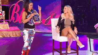 a woman is standing next to another woman who is sitting in a chair on a stage .