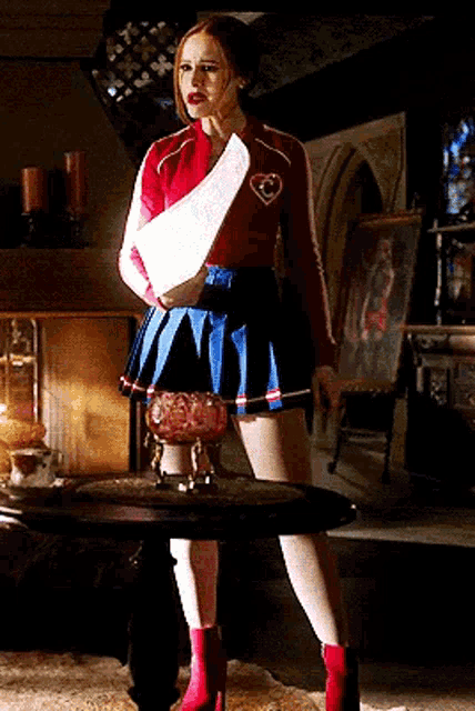 a woman in a cheerleader costume is standing next to a table in a living room holding a piece of paper .