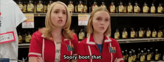 two women wearing red jackets that say sorry boot that are standing in front of a shelf of syrup