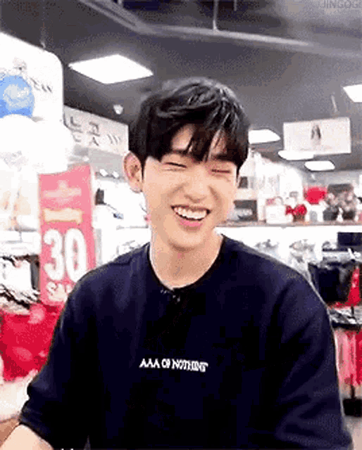 a young man wearing a black t-shirt is smiling while sitting in a store .