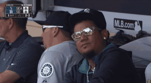 a man wearing sunglasses sits in the dugout watching a baseball game between the seahawks and the dodgers