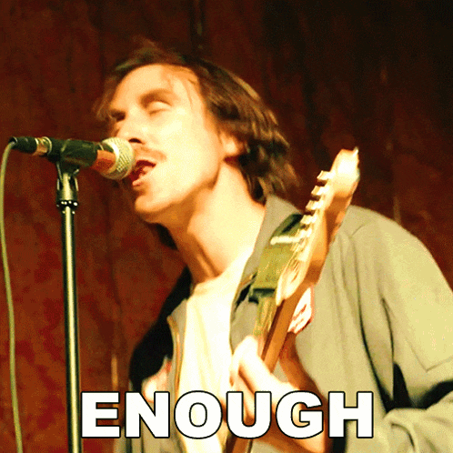a man singing into a microphone while holding a guitar with the word enough written above him