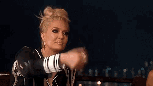 a woman in a bun is blowing a kiss at the camera while sitting at a table at night .