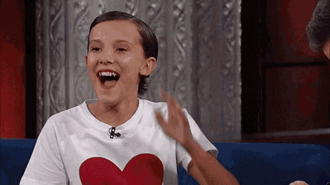 a young girl wearing a white shirt with a red heart on it is sitting on a blue couch .