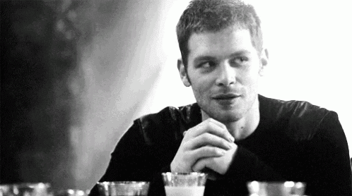 a black and white photo of a man sitting at a table with a glass of milk .