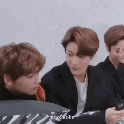 a group of young men are sitting next to each other and looking at a cell phone .