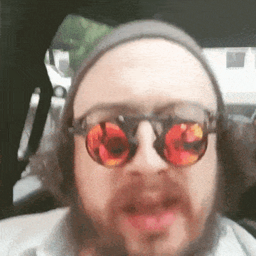 a man with a beard wearing sunglasses and a beanie is making a funny face