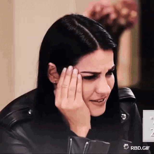 a woman in a leather jacket is crying with her hand on her forehead .
