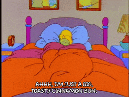 a cartoon of homer simpson laying in bed saying ahhh i 'm just a big toasty cinnamon bun.