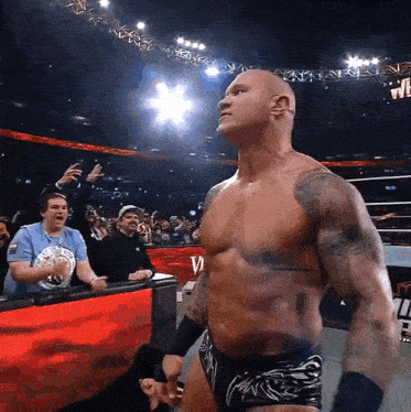 a shirtless wrestler stands in front of a crowd and a sign that says w on it