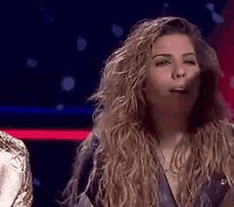 a woman with long curly hair is making a funny face while standing on a stage .