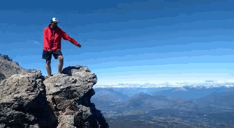 a man in a red jacket is standing on top of a rock