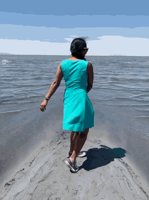 a woman in a blue dress is walking on a beach