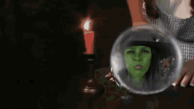 a woman with a green face is in a bubble with a red candle in the background