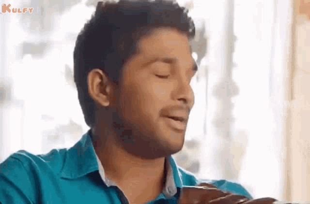 a man in a blue shirt is holding a piece of chocolate and making a funny face .