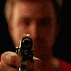 a man is pointing a gun at the camera with a blurry background .