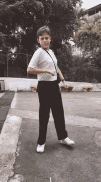 a young boy in a white shirt and black pants is dancing on a sidewalk .