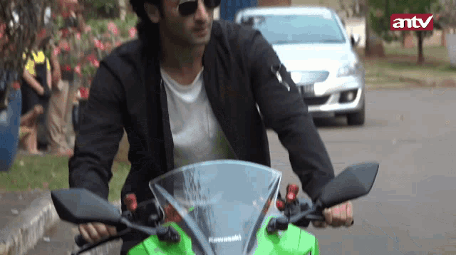 a man is riding a green kawasaki motorcycle with antv in the background