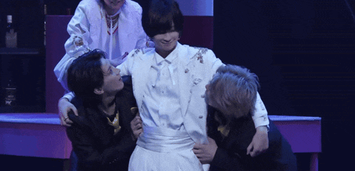 a group of people are hugging a man in a white suit on stage .