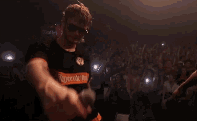 two men are dancing in front of a crowd with one wearing an orange shirt that says ' supreme ' on it
