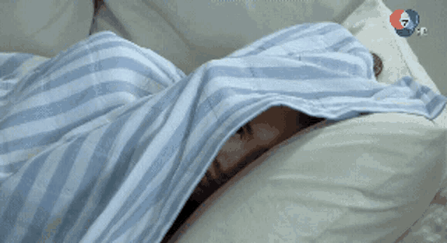 a person laying in bed with a blue and white striped blanket on