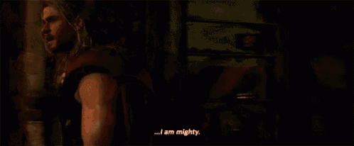 thor is standing in a dark room talking to a crowd of people .