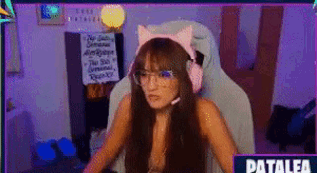 a woman wearing pink cat ears and glasses is sitting in a chair .