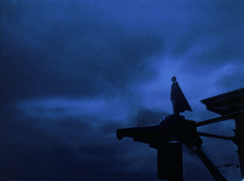 a man in a cape stands on top of a building in front of a circle with the number 6 on it