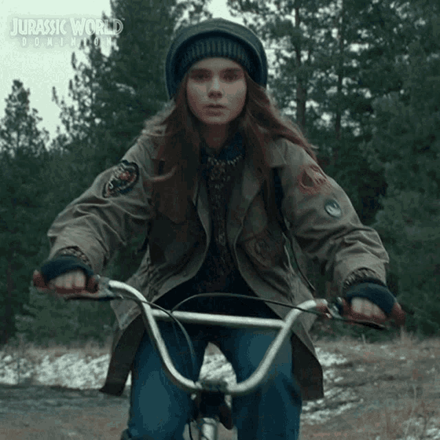 a girl is riding a bike with a jurassic world dominion poster in the background