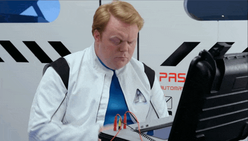 a man is sitting in front of a computer with the word pas on the wall behind him