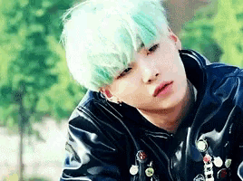 a young man with blue hair is wearing a black jacket and looking at the camera .