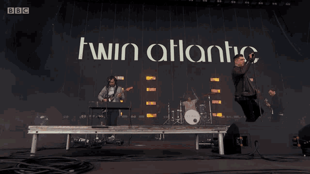 a man singing into a microphone in front of a banner that says twin atlantic