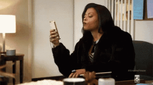 a woman is sitting at a desk holding a cell phone in her hand .