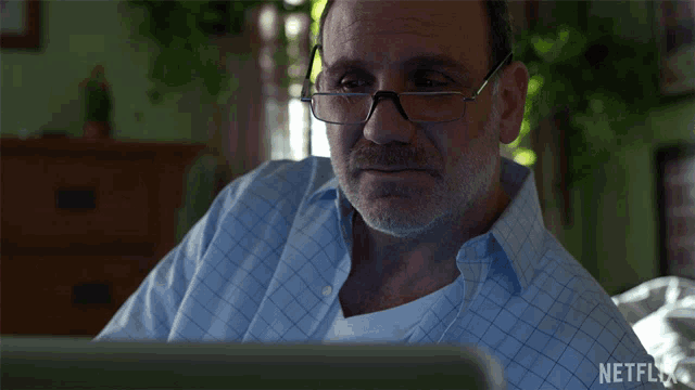 a man wearing glasses is looking at a laptop with netflix written on the bottom right