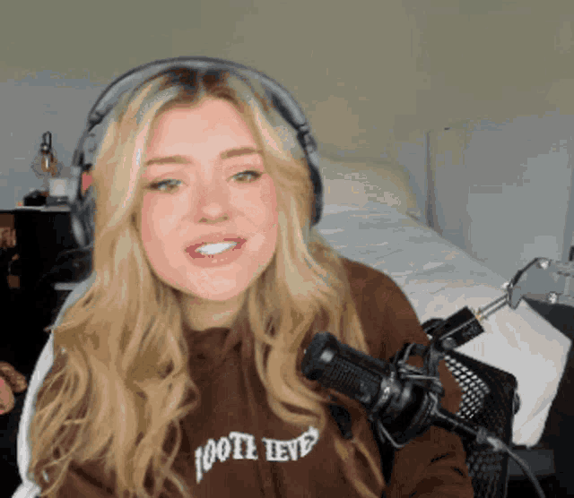 a woman wearing headphones and a sweatshirt that says 100th level is sitting in front of a microphone