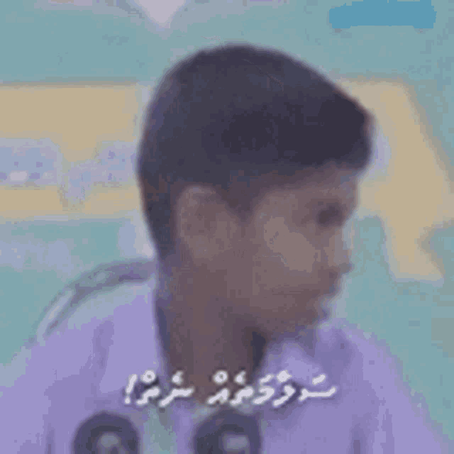 a young boy in a purple shirt is sitting in front of a microphone and making a funny face .