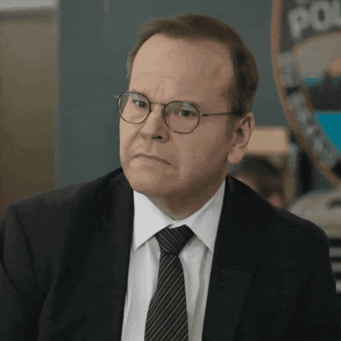 a man wearing glasses and a suit stands in front of a police sign