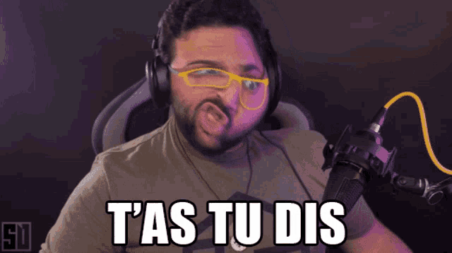 a man wearing headphones and glasses says t'as tu dis in front of a microphone