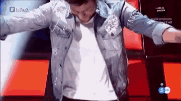 a man in a denim jacket is dancing on a stage