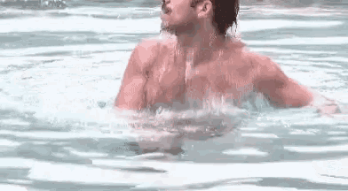 a shirtless man is swimming in a pool with his arms outstretched .