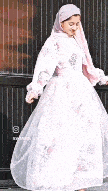 a woman wearing a white dress and a pink hijab is dancing