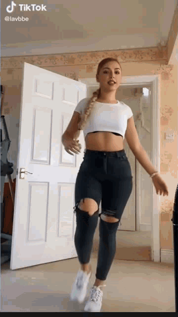 a woman in a crop top and ripped jeans is dancing in a room with a door open .