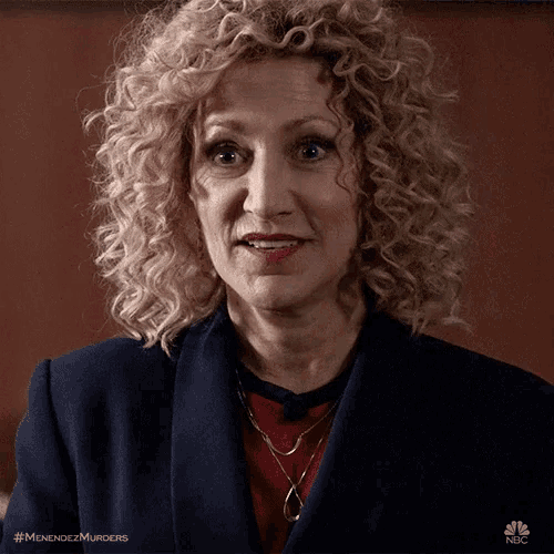 a woman with curly blonde hair is wearing a blue jacket and a red sweater .