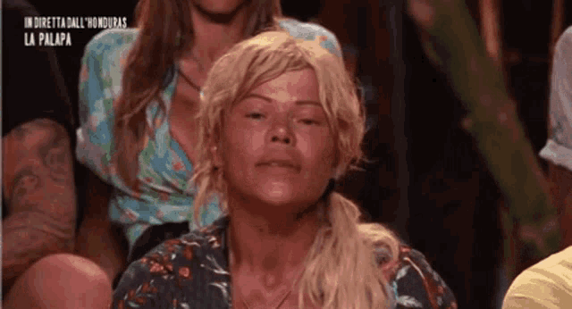 a woman wearing a blonde wig is sitting in a crowd .