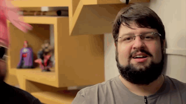 a man with glasses and a beard stands in front of a shelf with toys on it
