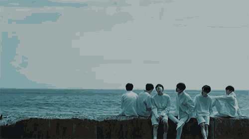 a group of young men are sitting on a ledge overlooking the ocean .