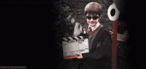 a man in a harry potter costume is holding a clapper board in a dark room .
